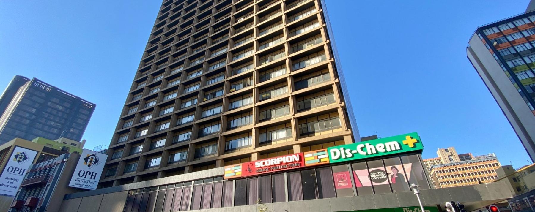 Tall commercial office tower with street-level retail and blue sky backdrop